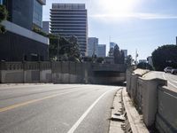 cars travel down an empty road near a city under a bridge and other buildings from which to the right is a pedestrian