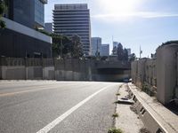 cars travel down an empty road near a city under a bridge and other buildings from which to the right is a pedestrian