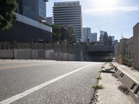 cars travel down an empty road near a city under a bridge and other buildings from which to the right is a pedestrian