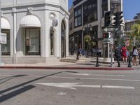 people cross the street in front of a building on a sunny day of the year