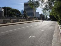 a very empty city street near some tall buildings or buildings with lots of trees in the middle