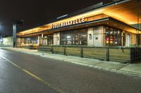 an outside restaurant with the outside lights on at night time near a street and cars