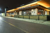 an outside restaurant with the outside lights on at night time near a street and cars