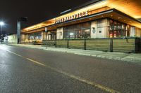 an outside restaurant with the outside lights on at night time near a street and cars