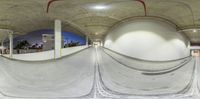 a view from a fisheye lens of a skateboard ramp with the lights on and a person jumping up in front