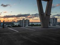 an empty parking lot with tall buildings in the background at sunset, surrounded by a boardwalk