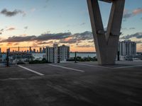 an empty parking lot with tall buildings in the background at sunset, surrounded by a boardwalk