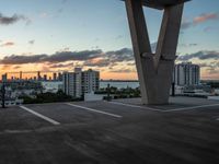 an empty parking lot with tall buildings in the background at sunset, surrounded by a boardwalk