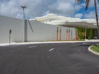 this is the empty parking lot of a large white building near a palm tree lined street