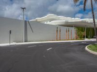 this is the empty parking lot of a large white building near a palm tree lined street