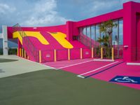 a tennis court with stairs, parking space and a pink structure in the middle of it