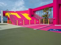 a tennis court with stairs, parking space and a pink structure in the middle of it