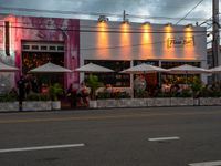 the front of an establishment with tables and umbrellas sitting outside it on a street