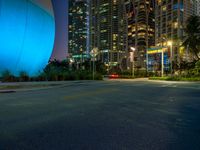 a city street at night with buildings in the background with a bright blue and white sphere behind