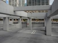 several parking spaces with concrete walls in the background with high rise buildings behind them and parking spaces under the roof