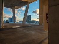 a empty parking lot next to an open sidewalk with buildings in the distance at sunset