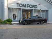 a black car parked in front of a tom ford store on a street corner with a building and bushes