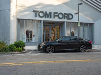 a black car parked in front of a tom ford store on a street corner with a building and bushes