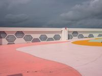 an outside basketball court with a cloudy sky over it and lots of different colored floors