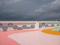 an outside basketball court with a cloudy sky over it and lots of different colored floors