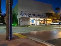 an empty street at night with people sitting on the curb and looking at the wall