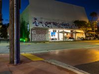 an empty street at night with people sitting on the curb and looking at the wall