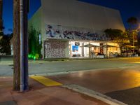 an empty street at night with people sitting on the curb and looking at the wall