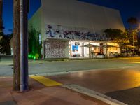 an empty street at night with people sitting on the curb and looking at the wall