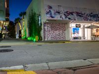 an empty street in front of a store lit up at night with street lights and trees growing out the corner