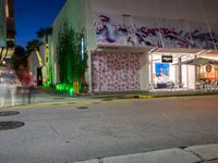 an empty street in front of a store lit up at night with street lights and trees growing out the corner