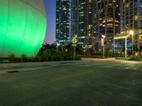 there is a big green ball in the middle of the street with tall buildings in the background