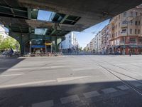 a street with two trains on it and a few people walking under an overpass