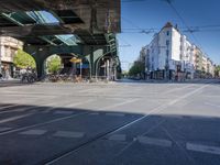 a street with two trains on it and a few people walking under an overpass