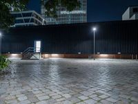 a brick paver and steps at night with light poles around it and some tall building