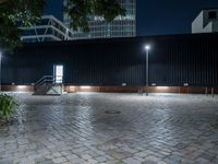 a brick paver and steps at night with light poles around it and some tall building