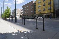 there are some black pole mounted to the sidewalk near the buildings in the city with cars parked at the street corner