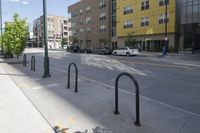 there are some black pole mounted to the sidewalk near the buildings in the city with cars parked at the street corner