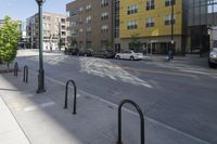 there are some black pole mounted to the sidewalk near the buildings in the city with cars parked at the street corner