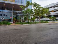 a large parking lot surrounded by a parking lot next to a tall white building with a tree in front of it