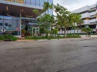 a large parking lot surrounded by a parking lot next to a tall white building with a tree in front of it