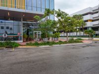 a large parking lot surrounded by a parking lot next to a tall white building with a tree in front of it