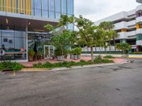 a large parking lot surrounded by a parking lot next to a tall white building with a tree in front of it