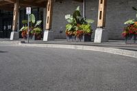 some flowers and potted plants line a paved driveway next to a building with wooden posts