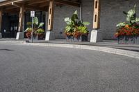 some flowers and potted plants line a paved driveway next to a building with wooden posts