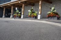 some flowers and potted plants line a paved driveway next to a building with wooden posts