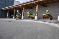 some flowers and potted plants line a paved driveway next to a building with wooden posts