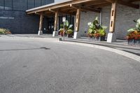 some flowers and potted plants line a paved driveway next to a building with wooden posts