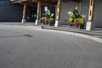 some flowers and potted plants line a paved driveway next to a building with wooden posts