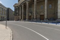 an empty road with columns around it and two people walking by and building behind it