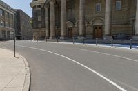 an empty road with columns around it and two people walking by and building behind it